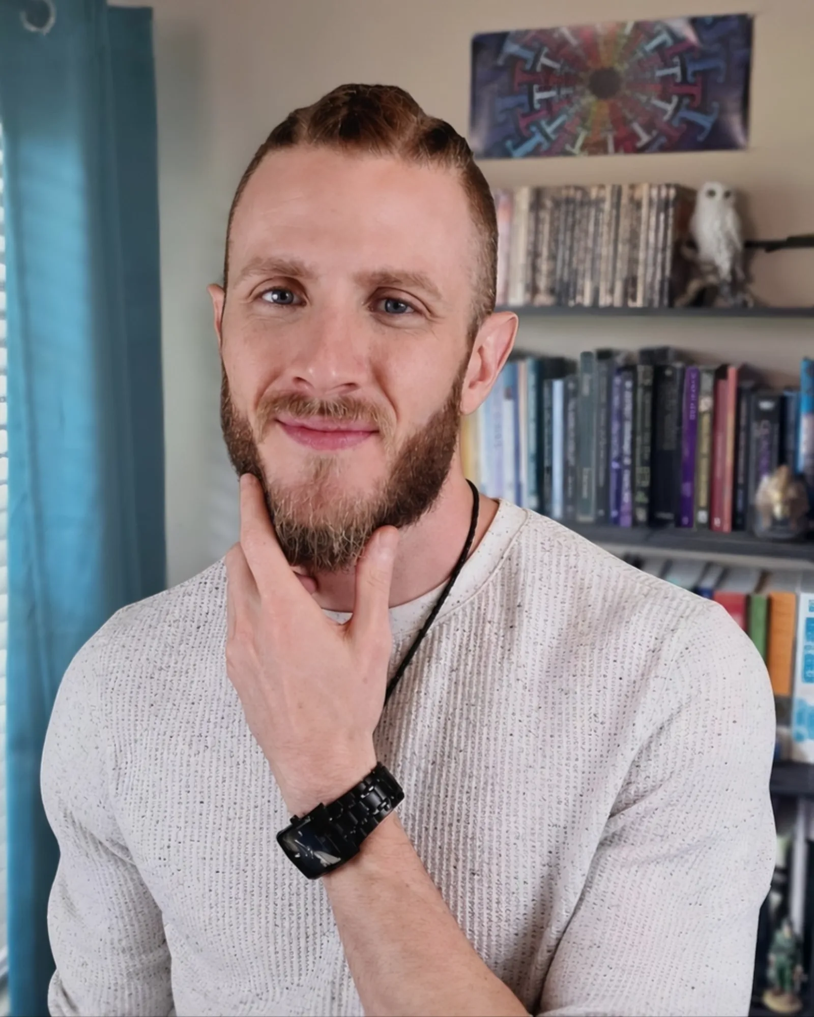 Logan Hart, who built Sondor: a bearded man in a cream knit sweater, resting his chin on his hand and smiling slightly, in front of shelves of books.